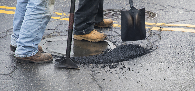 Pothole Near Sewer Cover Being Filled by Two DPW&P Workers