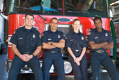 Four Fire Fighters Sitting on Front Bumper of Fire Engine in Garage