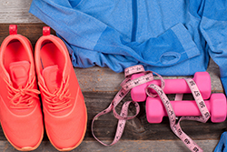 Pink Dumbells, Tennis Shoes and a Workout Shirt Lying on a Wooden Floor