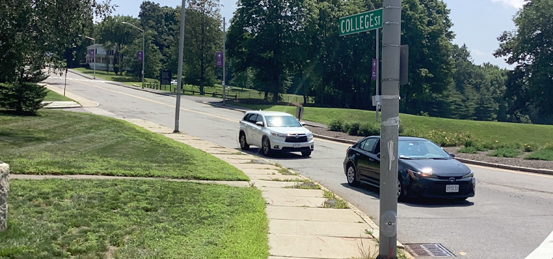 Stop Sign and Intersection at College Street Showing Two Cars in Roadway with Sidewalk and Grass on Left Side