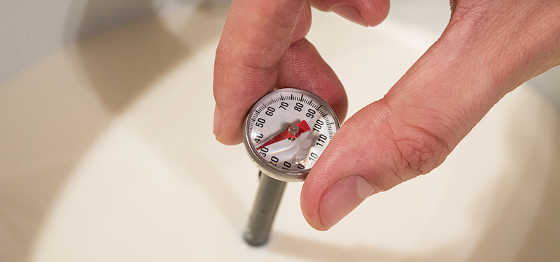 Hand Holding a Thermometer in a Large Container of Milk