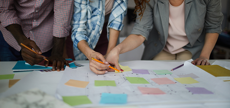 Closeup of creative business team working on design project focused on table with roadmap and colorful stickie notes.