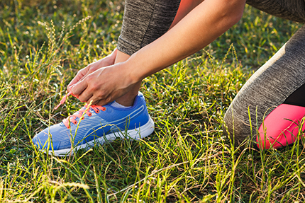 Woman in Workout Clothes Tying Her Shoe in the Grass