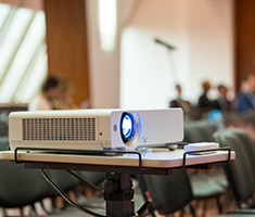 White Digital Projector Sitting on Table in a Room of People