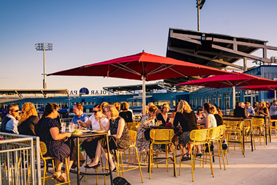 Group of People Sitting at Tables and Umbrellas on Upper Concourse of Polar Park