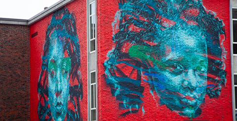 Mural on Building of Two Women's Faces in Blue Tones on Red Background