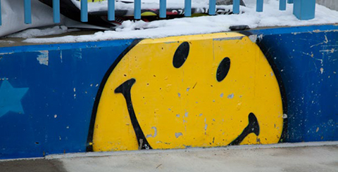 Yellow Smiley Face on Blue Background Painted on a Small Concrete Wall
