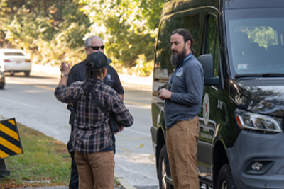 Two Workers/Volunteers Standing in Front of Black Van with WPD Officer