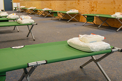 Rows of Green Cots in Open Shelter Space with Bedding and Hygiene Products on One Side