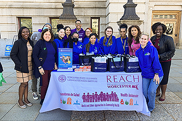 Group of Volunteers Standing Around Information Table for REACH on the Common