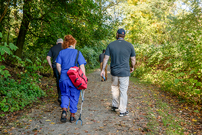 Group of Four Workers/Volunteers Walking on Wooded Trail Carrying Emergency Supplies