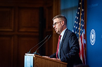 Man with Glasses in Blue Suit Standing at Podium Giving Welcome Speech
