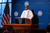 Pastor in White Garments at Podium Giving Opening Invocation to Attendees