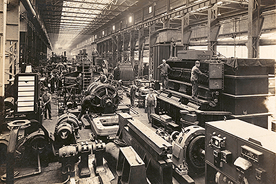 Black and White Photo of an Old Factory from Early 1900s with Worker Standing in Middle Looking at Camera