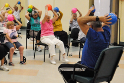 Group of Seniors Exercising with Medicine Balls Raised Above their Heads While Seated