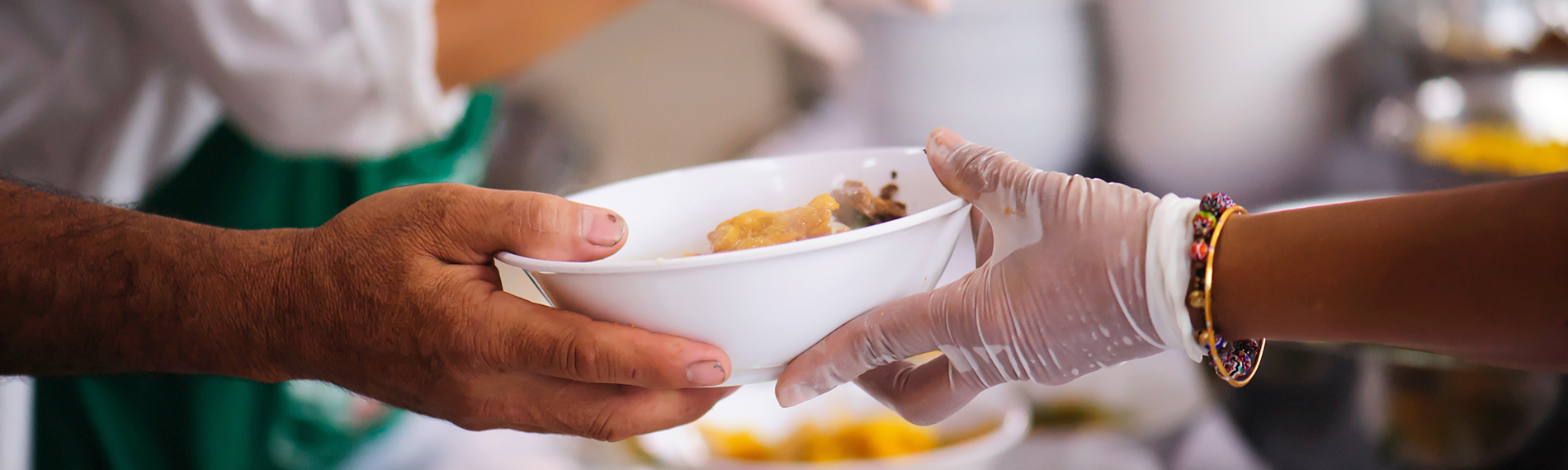 Volunteer Wearing Glove Serving White Bowl of Food to Someone at Community Kitchen