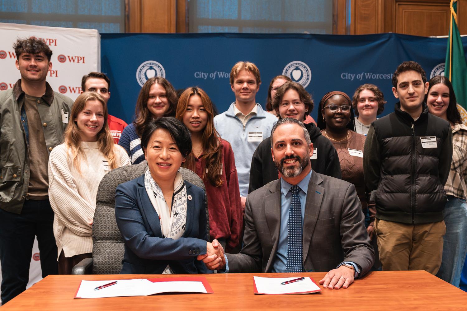 Photo of WPI President Grace Wang and City Manager Eric D. Batista shaking hands with WPI students behind them