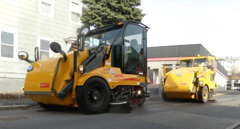 Two Yellow Street Sweepers In Line Working to Clean a City Street
