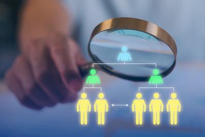 Hand Holding Magnifying Glass Looking at Icons of People in Yellow and Green