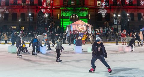 Group of People Ice Skating on the Oval at Night with Back of City Hall in the Background