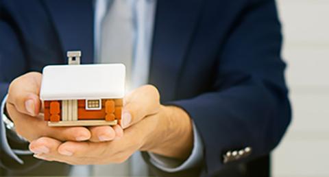 Business Man Holding a Wooden House in His Hands